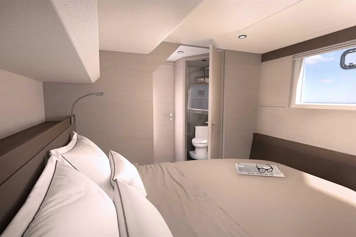 Modern interior of a boat cabin featuring a bed with pillows, an open bathroom door, and a window with ocean views.